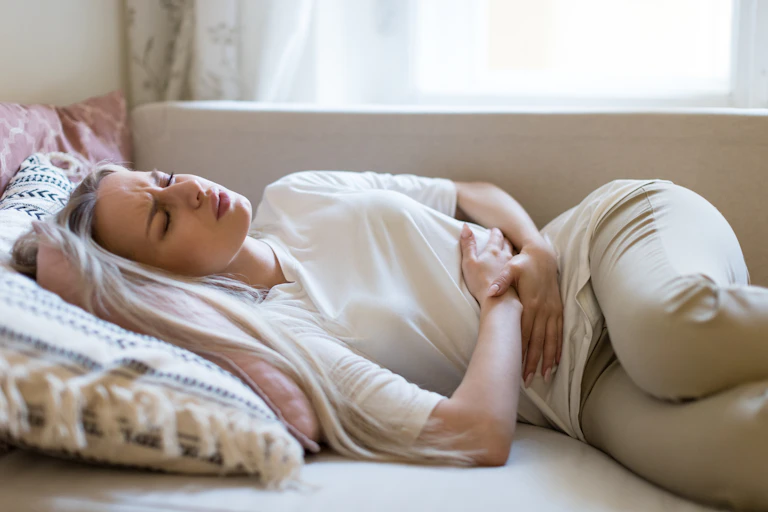 Woman lying on bed in pain and holding lower abdomen