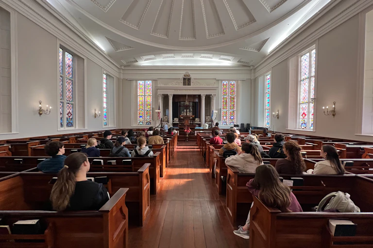 A religious sanctuary with stained-glass windows and young people sitting in wooden pews.