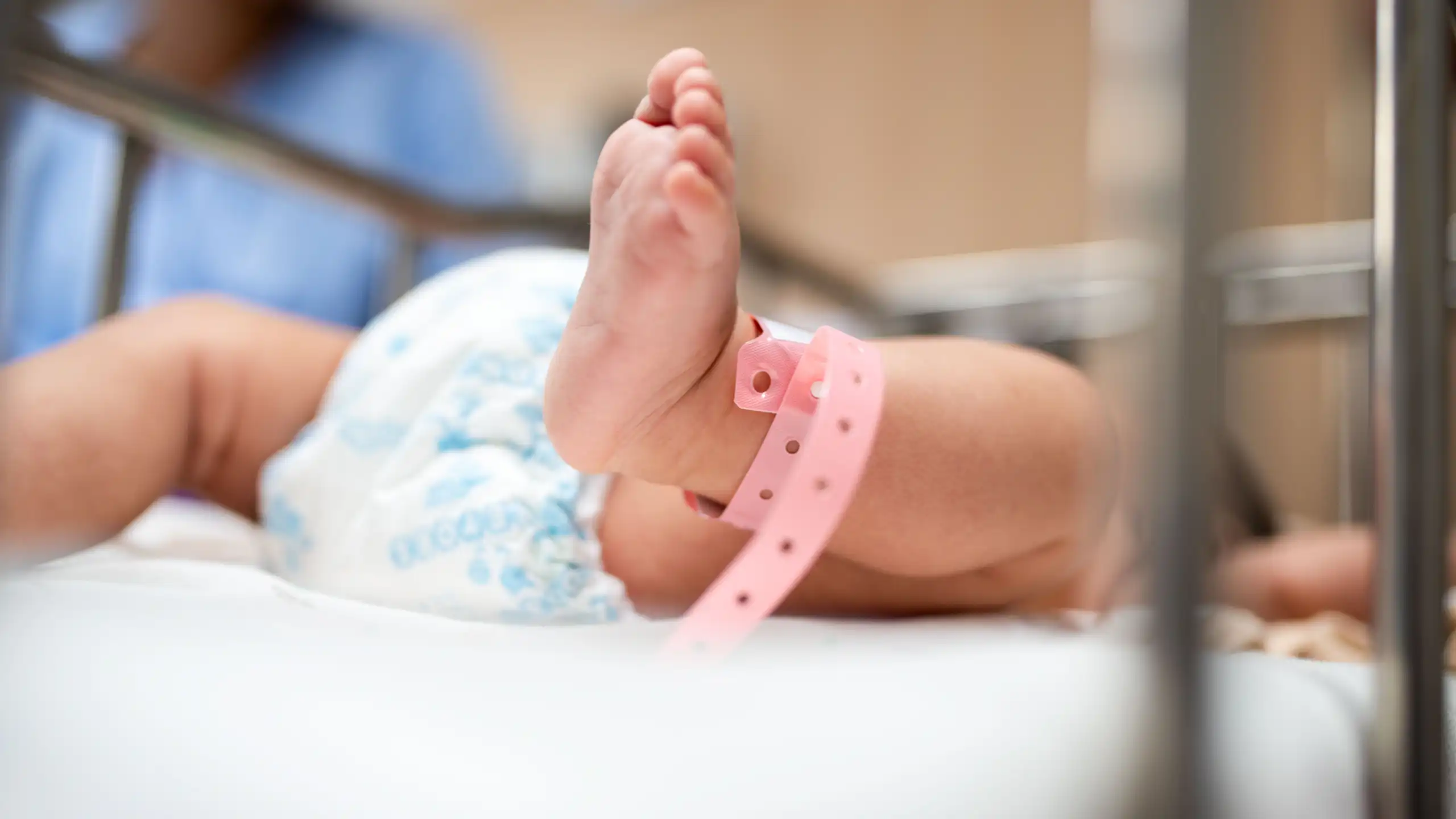 A close-up of a newborn baby’s feet, wearing a pink hospital wristband.
