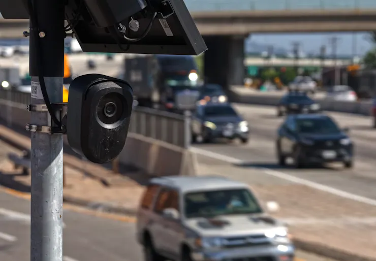 A camera on a post in seen as cars move along a highway in the background.