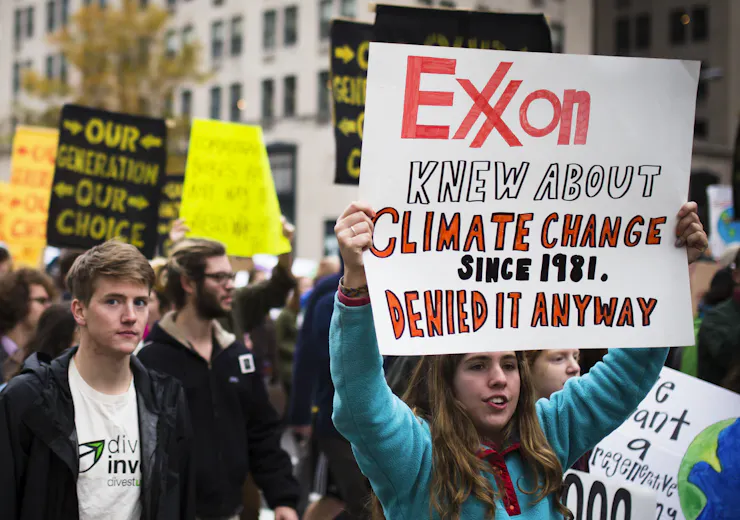 A group of people holding signs, including one reading 'Exxon knew about climate change since 1981, denied it anyway.'