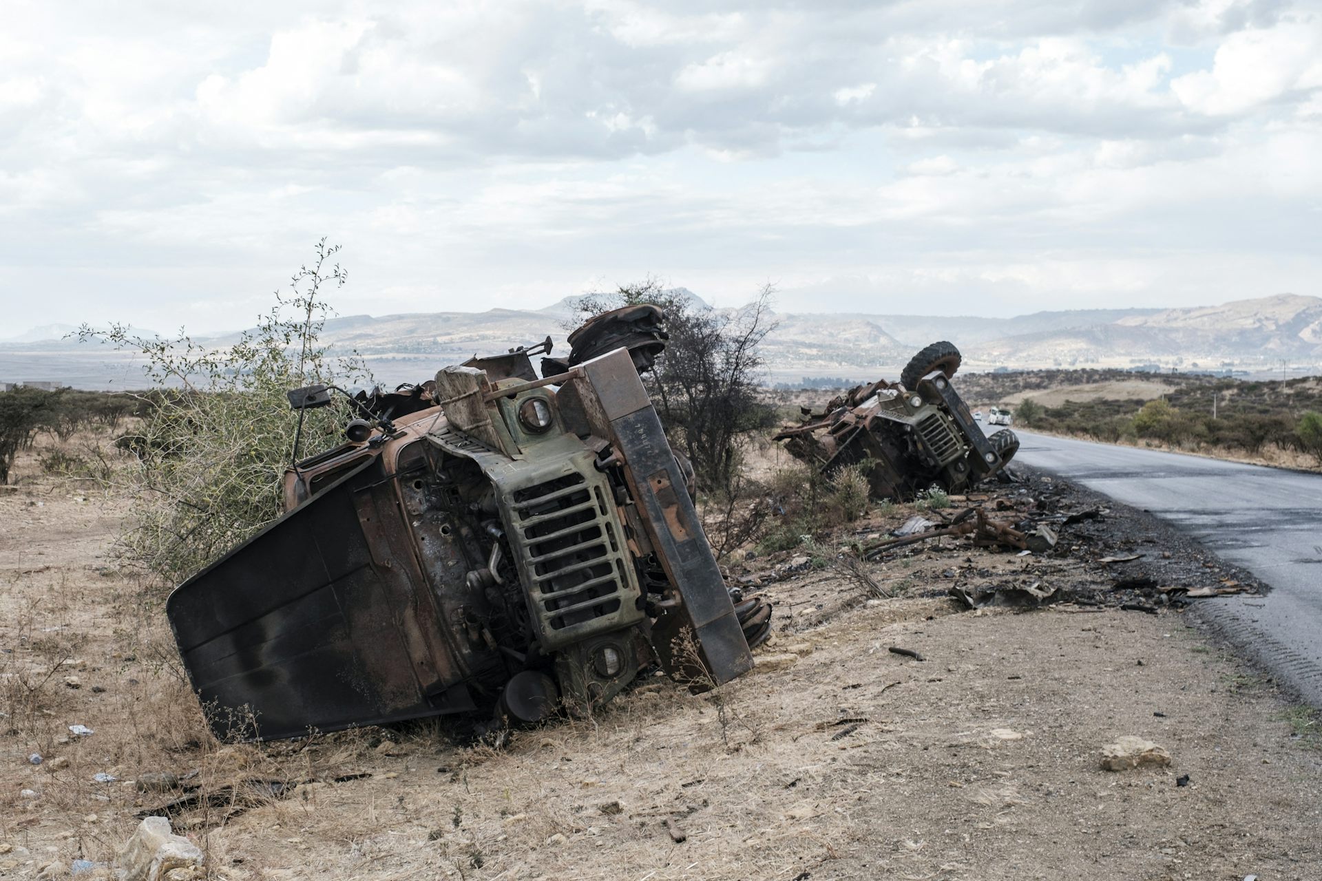 Destroyed vehicles are seen by the side of a road.