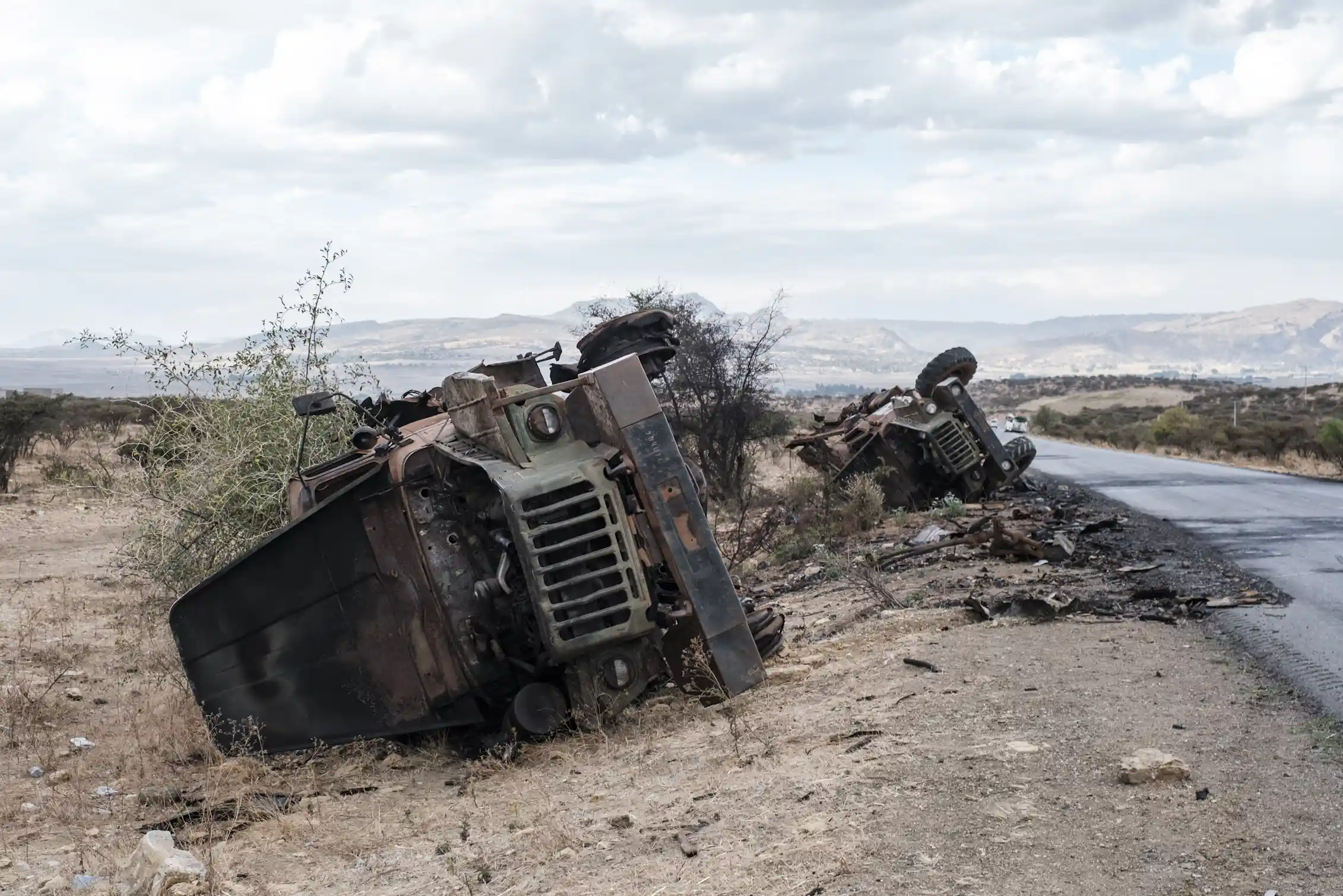 Destroyed vehicles are seen by the side of a road.