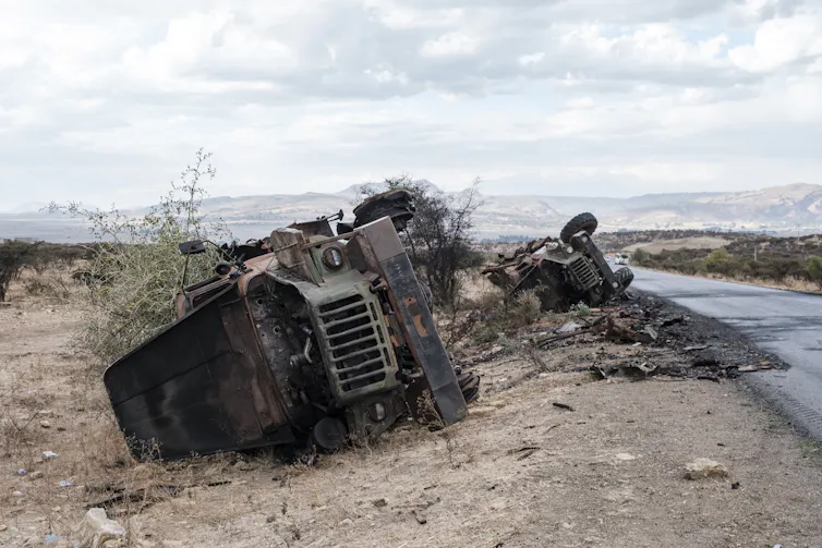 Destroyed vehicles are seen by the side of a road.