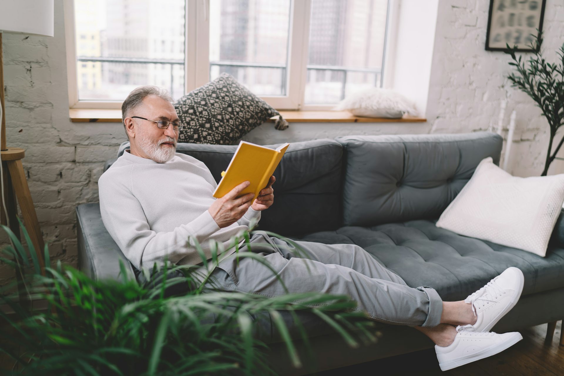 A man lazes on sofa reading a book and smiling with pleasure