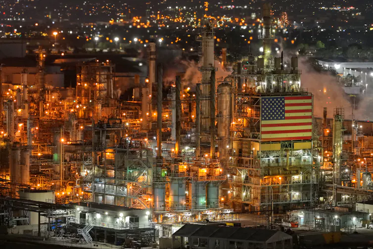 An industrial area is viewed from the air, showing lights and tubes and pipes and metal buildings.