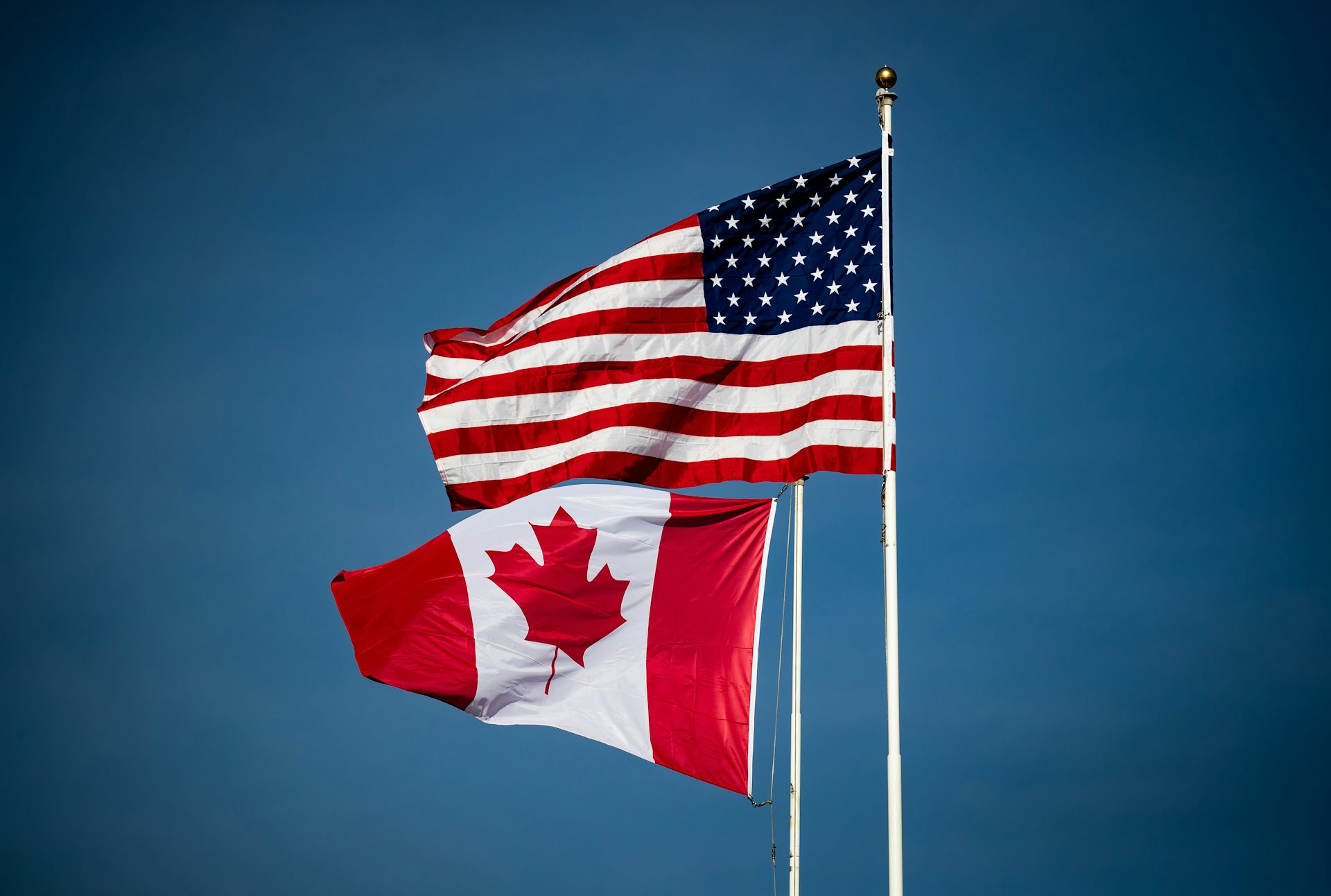 Un drapeau canadien et un drapeau américain flottent au vent.