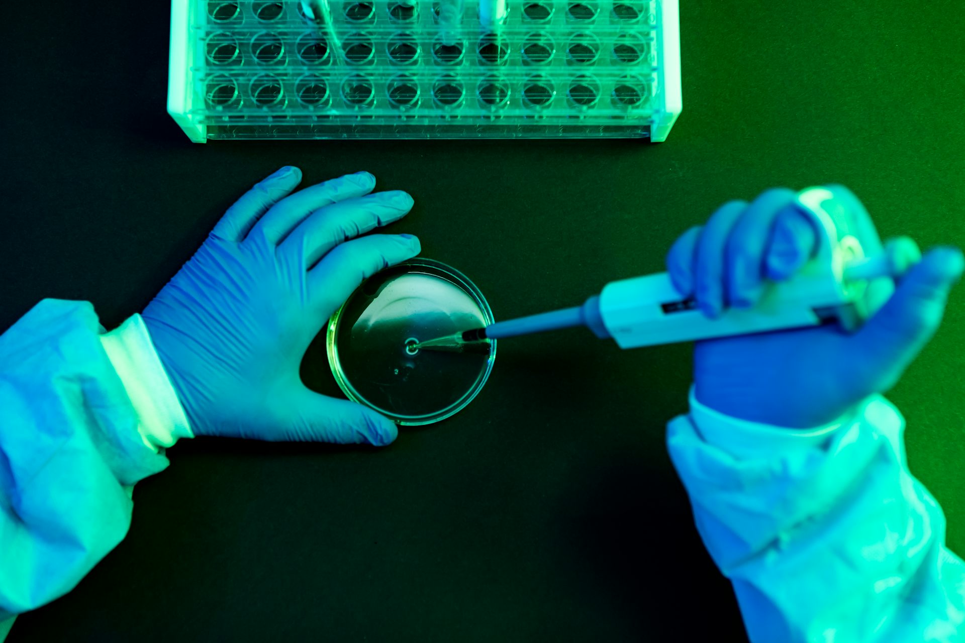 Mãos com luvas manuseiam uma pipeta em um laboratório.