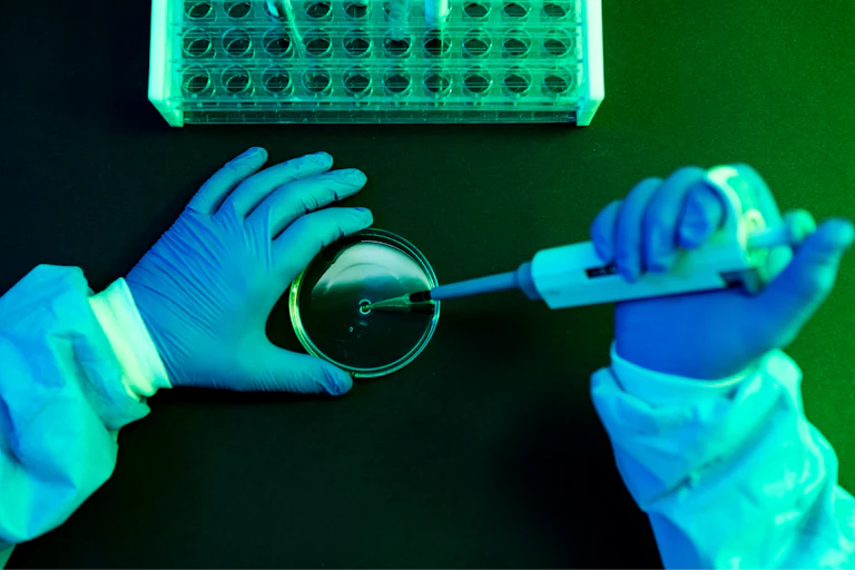 Mãos com luvas manuseiam uma pipeta em um laboratório.