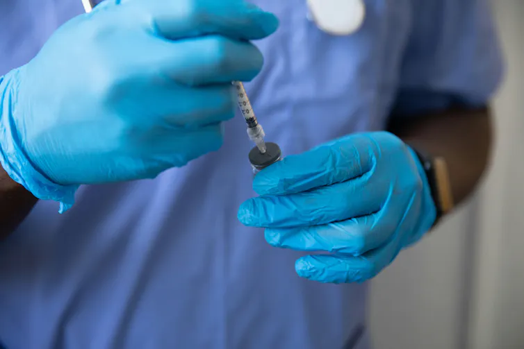 Gloved hands holding a syringe and glass vial