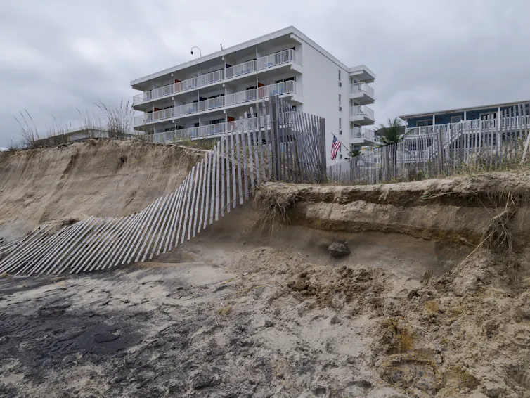 A tall residential building with a partially collapsed and eroded dune.