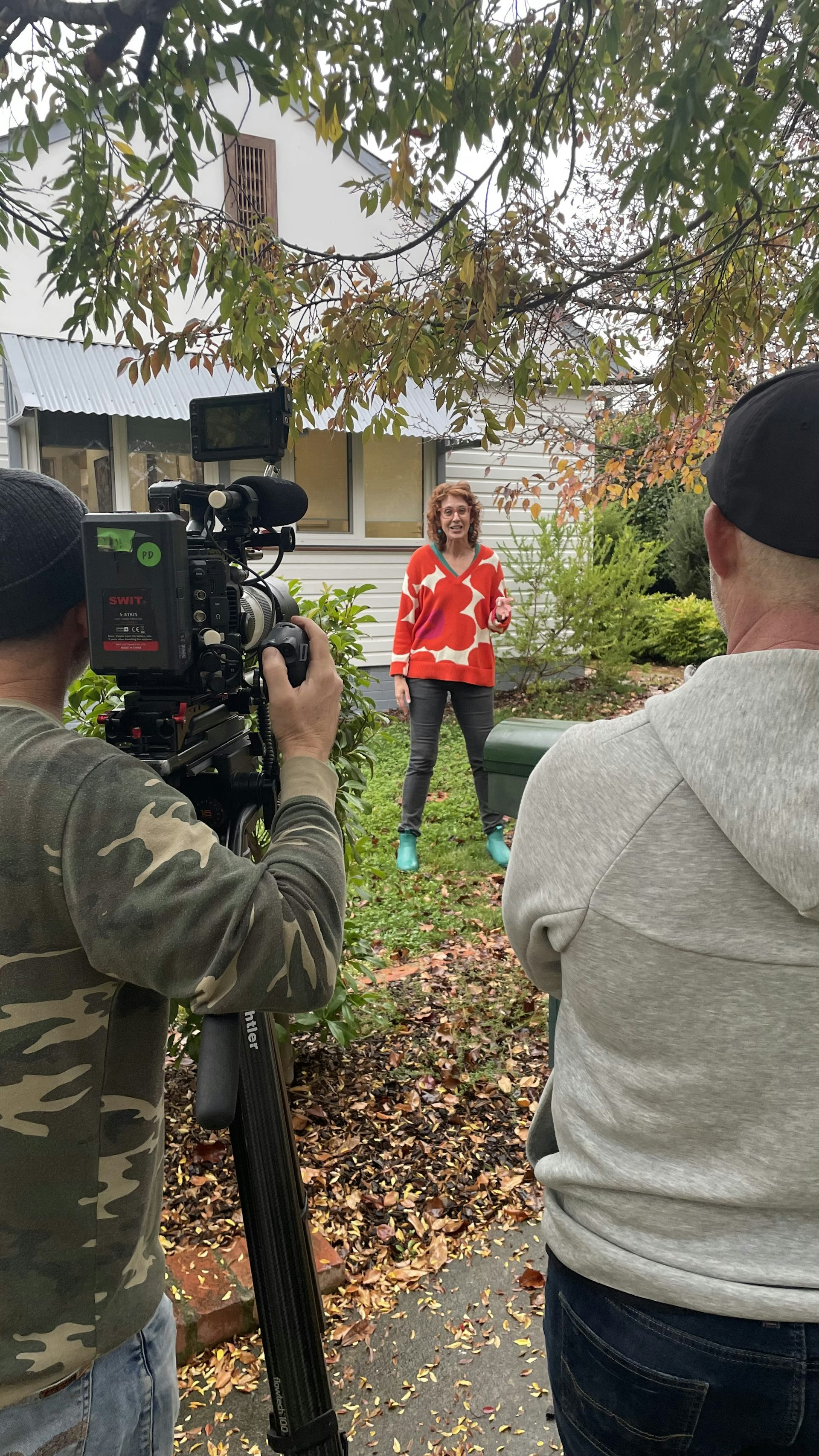 A woman stands in a garden while being filmed on camera.