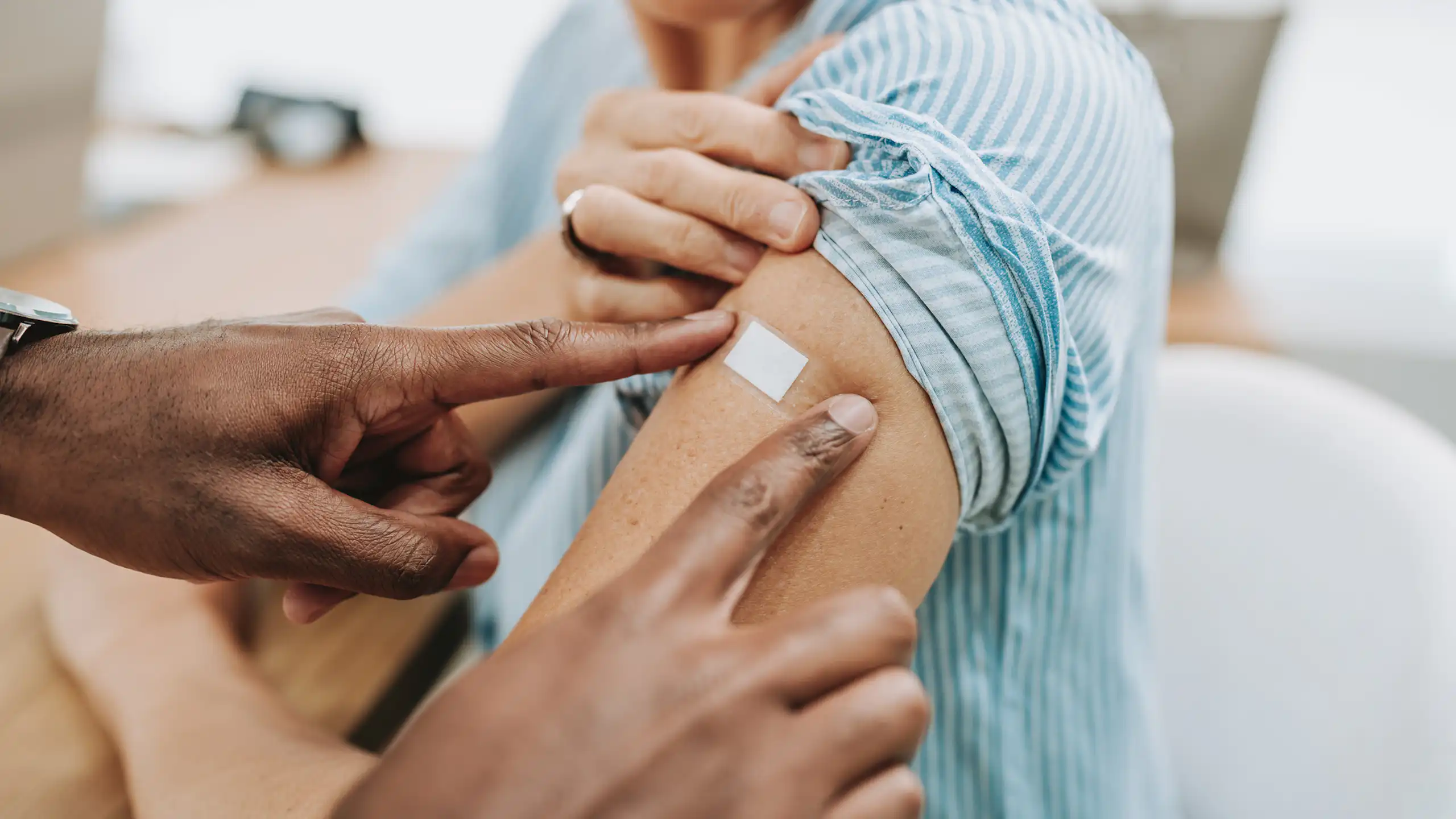 Health professional placing Bandaid over upper arm of woman after vaccination