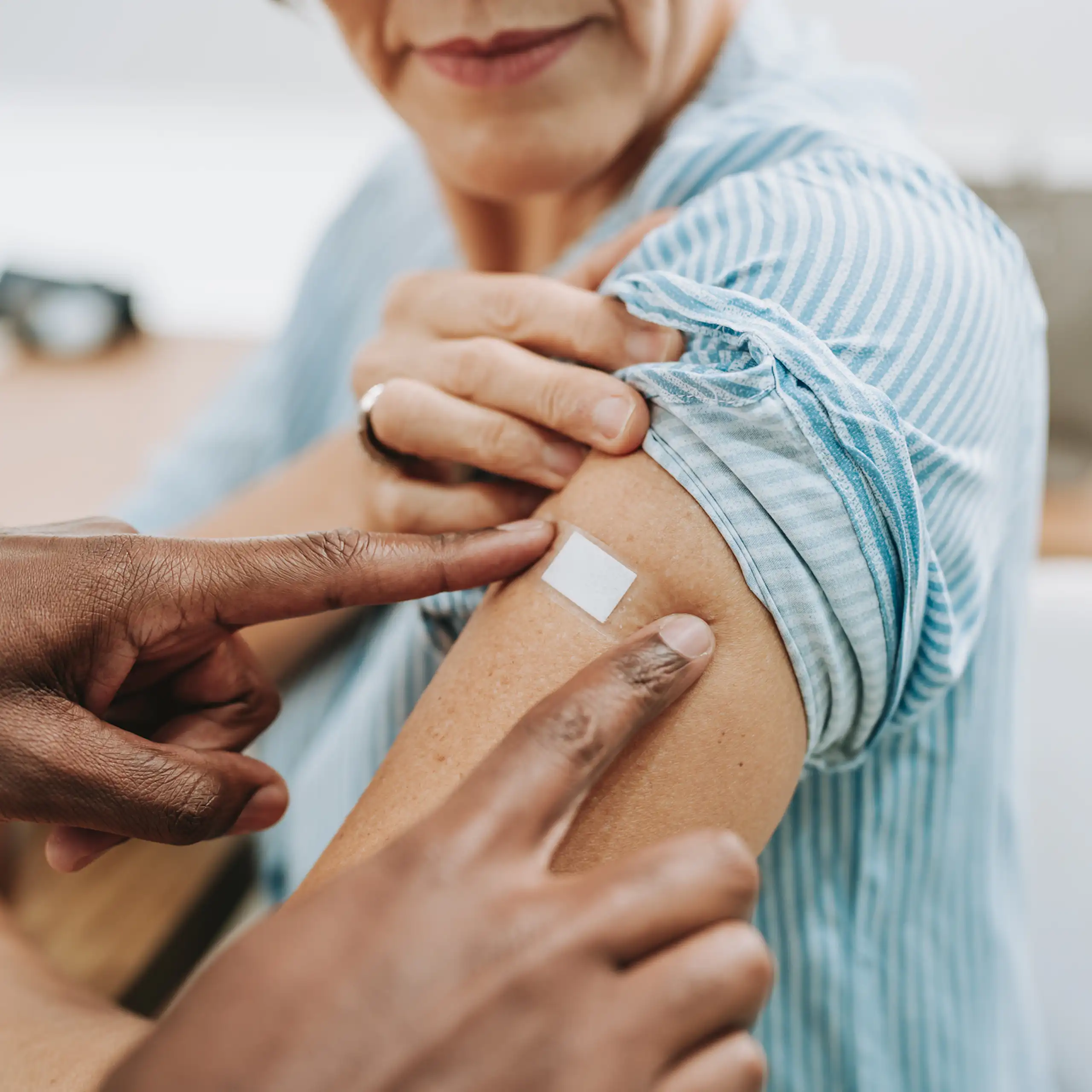 Health professional placing Bandaid over upper arm of woman after vaccination