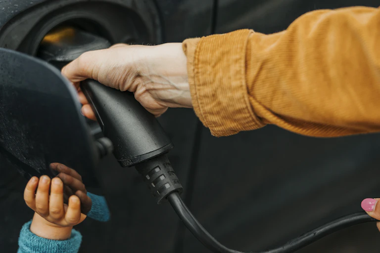 A woman's hand plugs a charger into a port, helped by a child's hand.