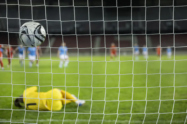 A soccer ball lodges in the white net after a successful shot on goal