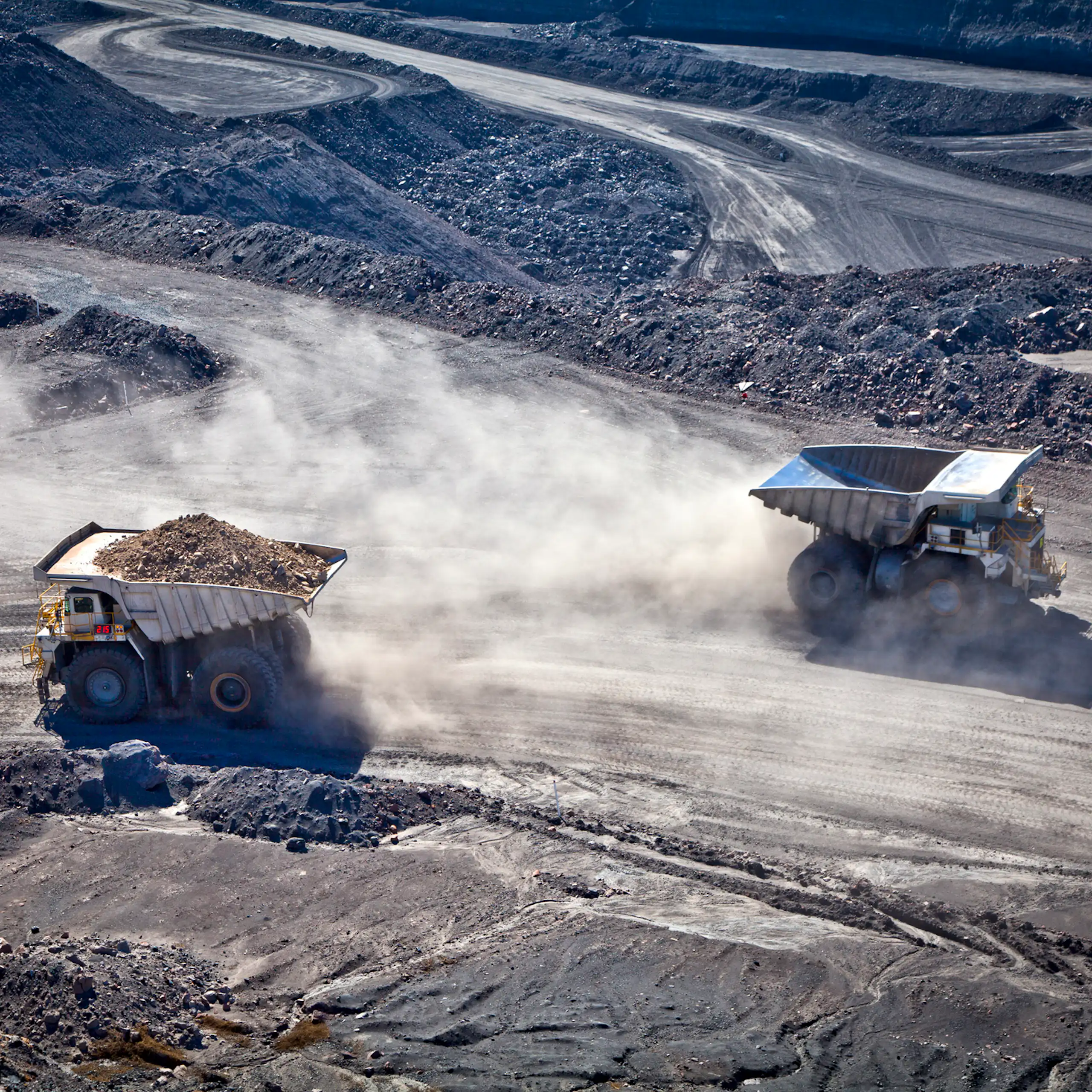 Two trucks haul ore or coal from a mine.