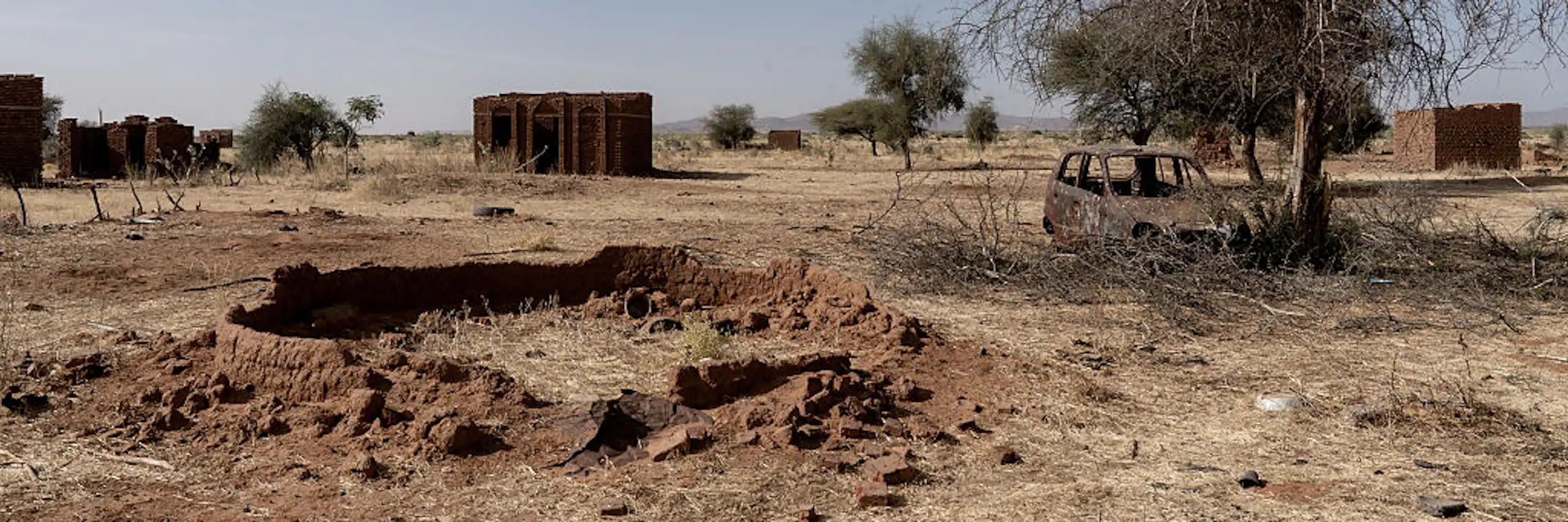 A view of a few empty homes and burnt out vehicle in a field