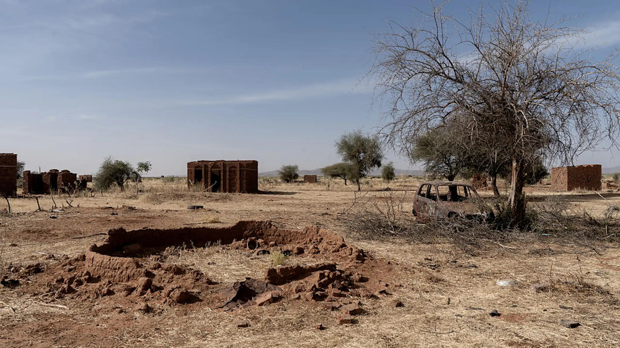 A view of a few empty homes and burnt out vehicle in a field