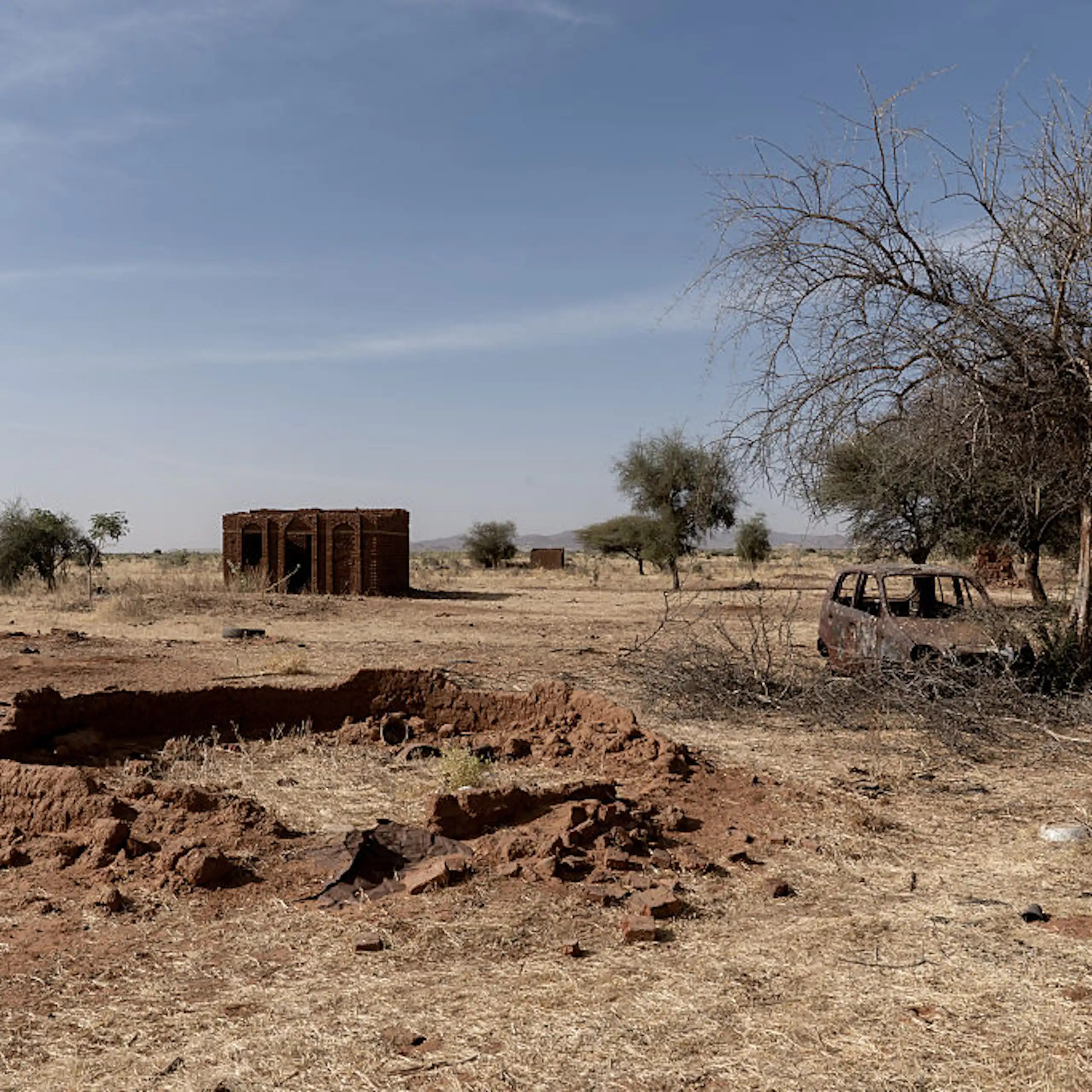 A view of a few empty homes and burnt out vehicle in a field