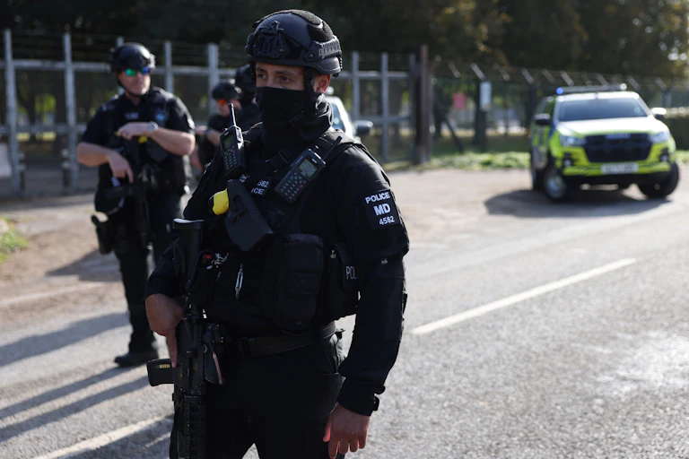 armed police stand in front of the perimeter fence at raf fairford with a police car in the background