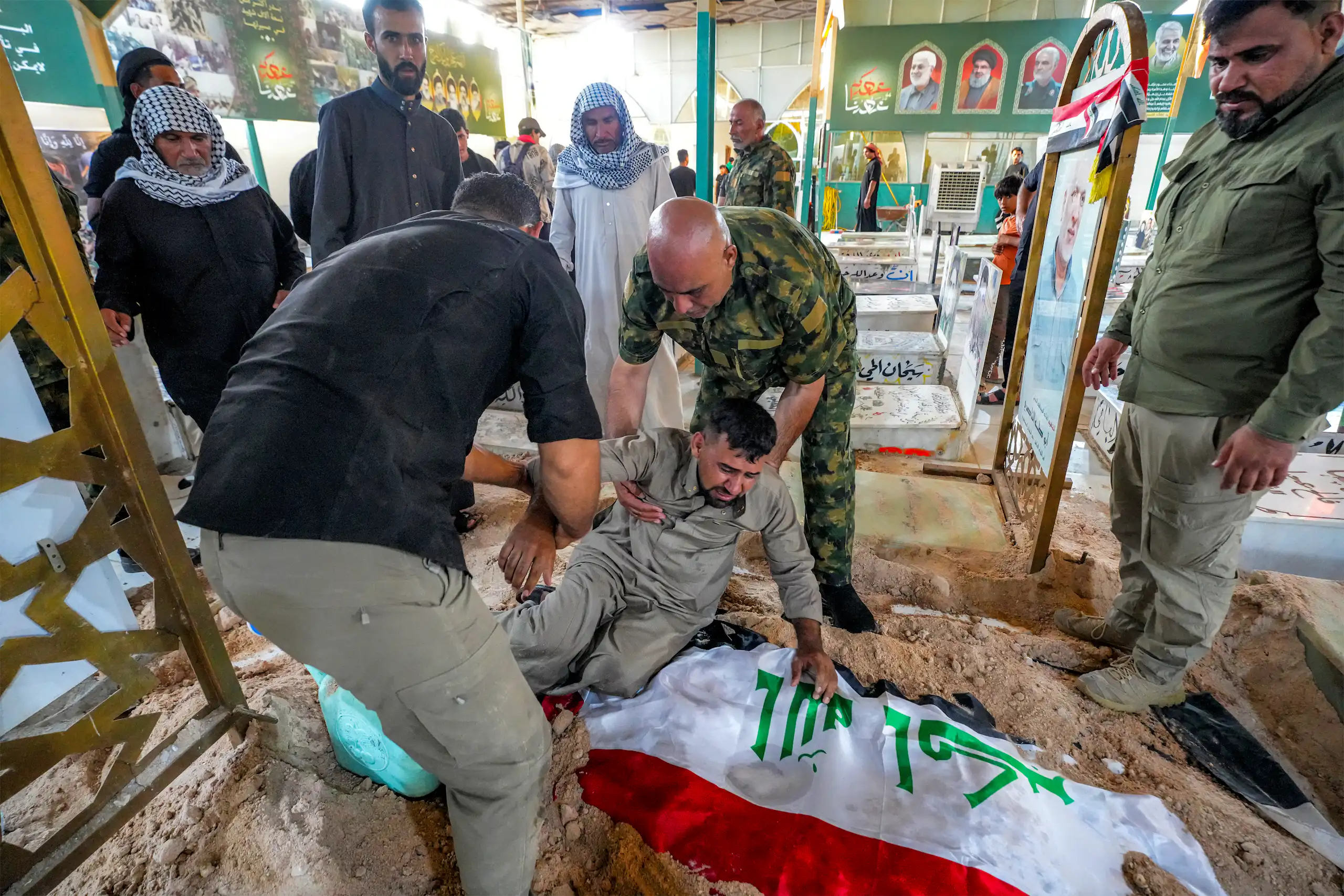 Un milicien pleure effondré sur un linceul recouvert du drapeau irakien, deux autres tentent de le relever.