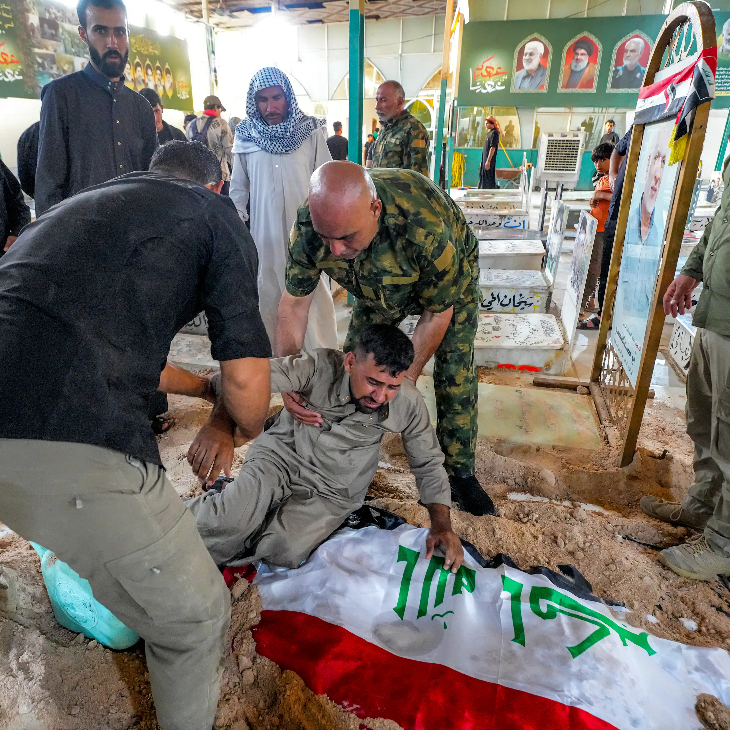 Un milicien pleure effondré sur un linceul recouvert du drapeau irakien, deux autres tentent de le relever.