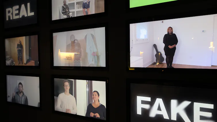 A wall of video screens shows various images, with the word 'REAL' in the upper left corner and 'FAKE' in the lower right.