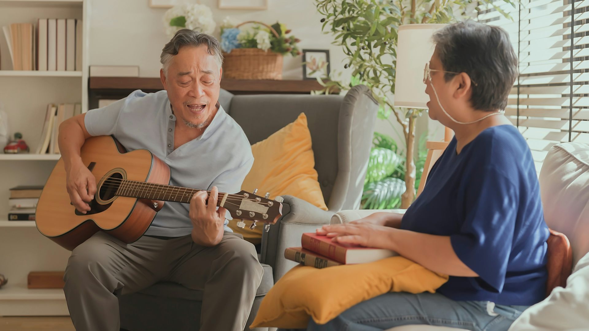 An elderly man plays an acoustic guitar while an elderly woman sings along.