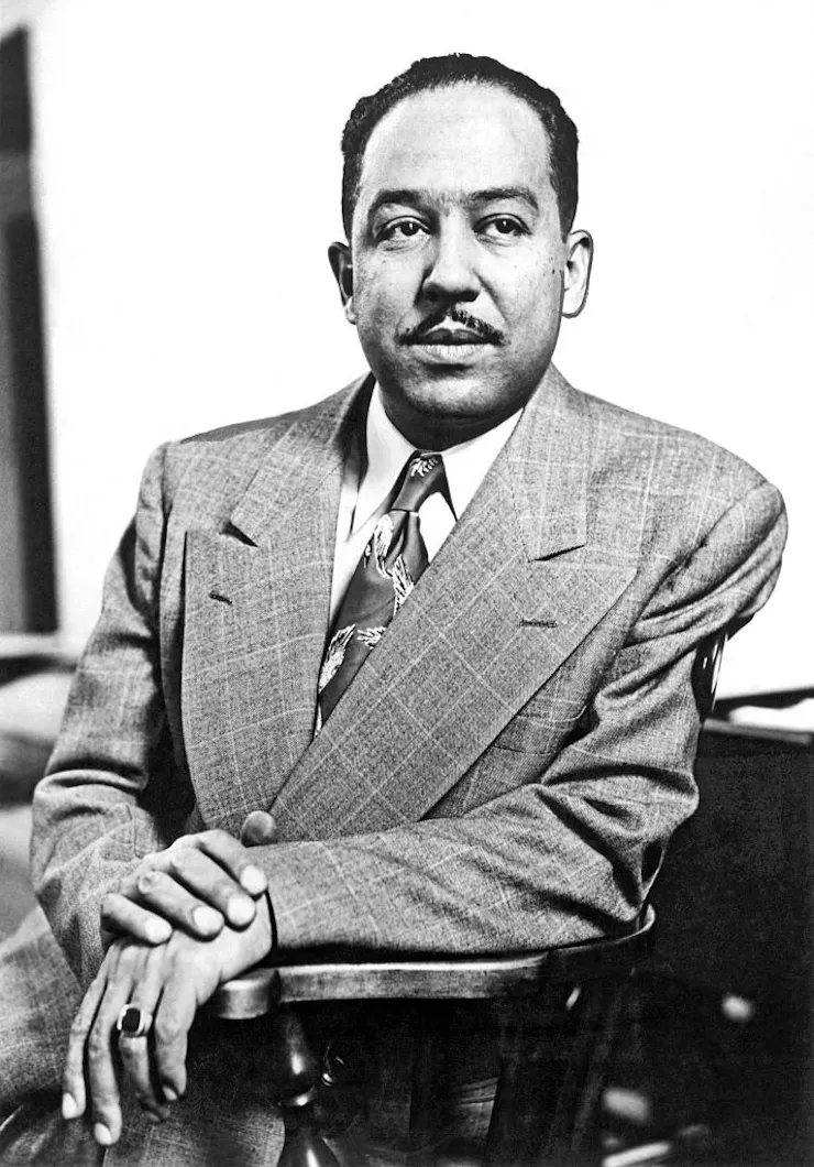 Middle-aged mixed-race man with a thin mustache posing while wearing a suit and sitting in a wooden chair.