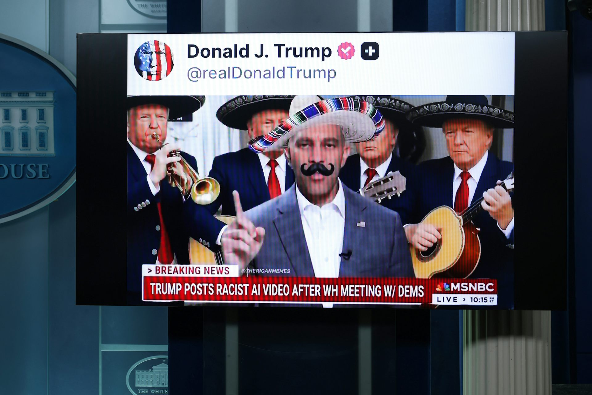 A screen in a press briefing room shows a social media video of a man in a sombrero and fake mustache, flanked by mariachi musicians, above a cable news banner.
