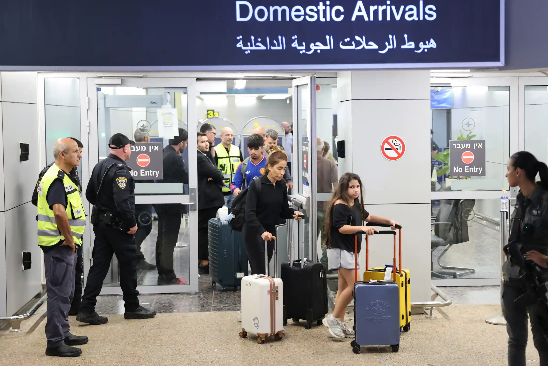 Passengers pushing luggage walk under a sign that says
