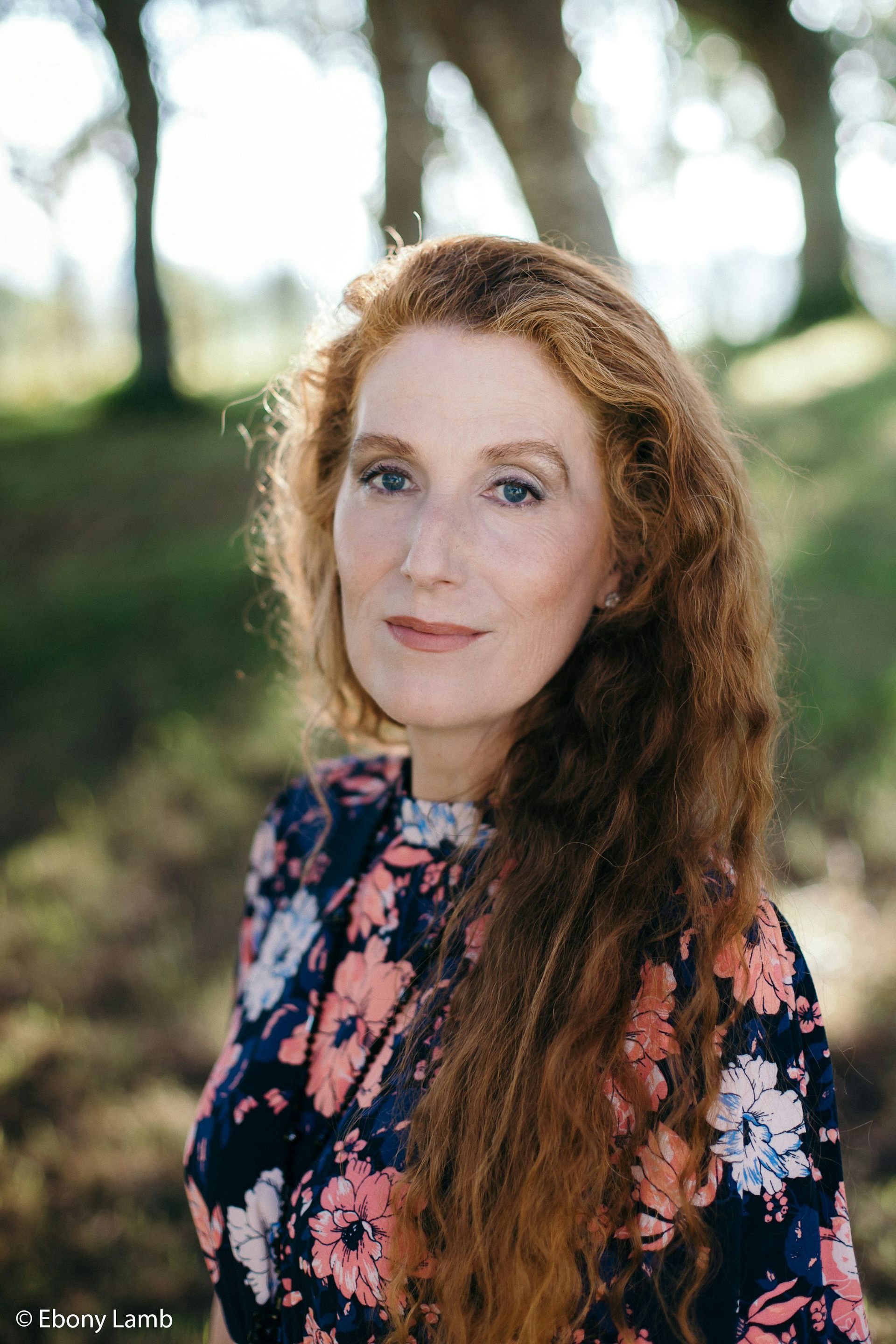 A woman with long red hair and a floral dress