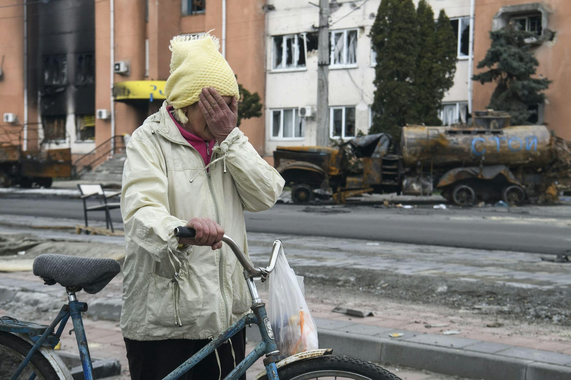 A woman pushing a bicycle and covering her eyes with her hand.