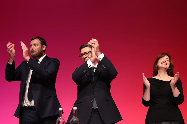 Andy Burnham and two colleagues applaud.