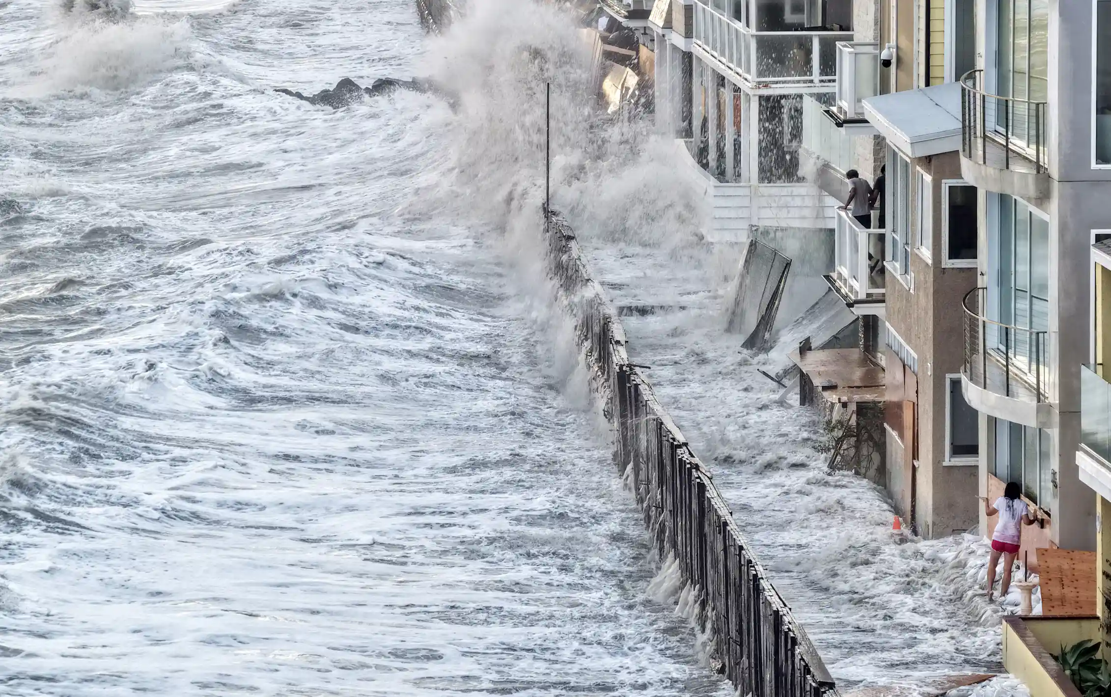 Water laps up against homes along the coast, including inside a temporary barrier created to protect them.
