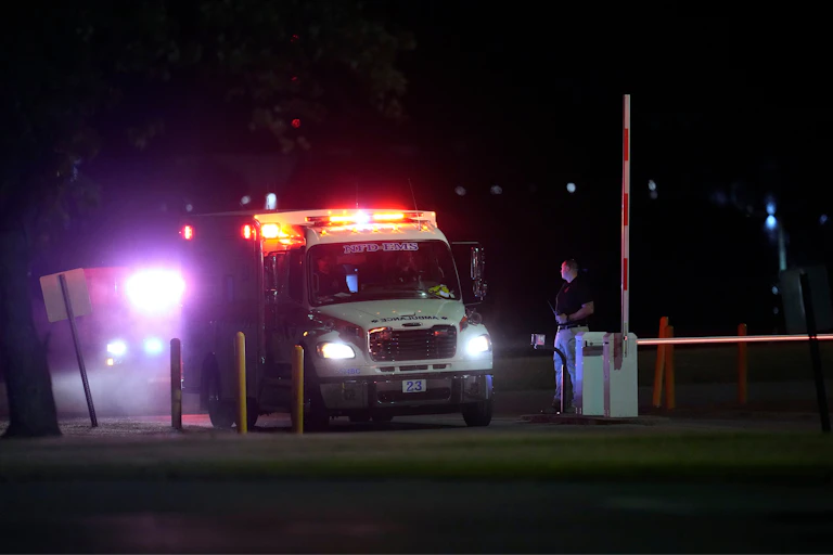 An ambulance drives through a gated entrance at night.