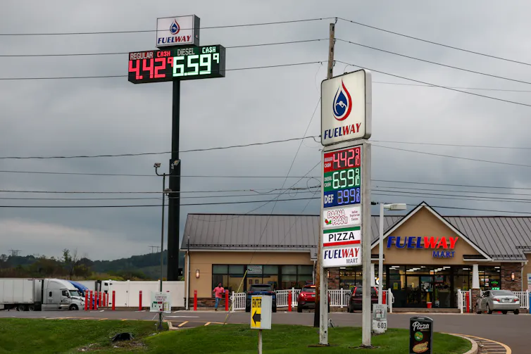 A large sign displays gas prices near a strip mall