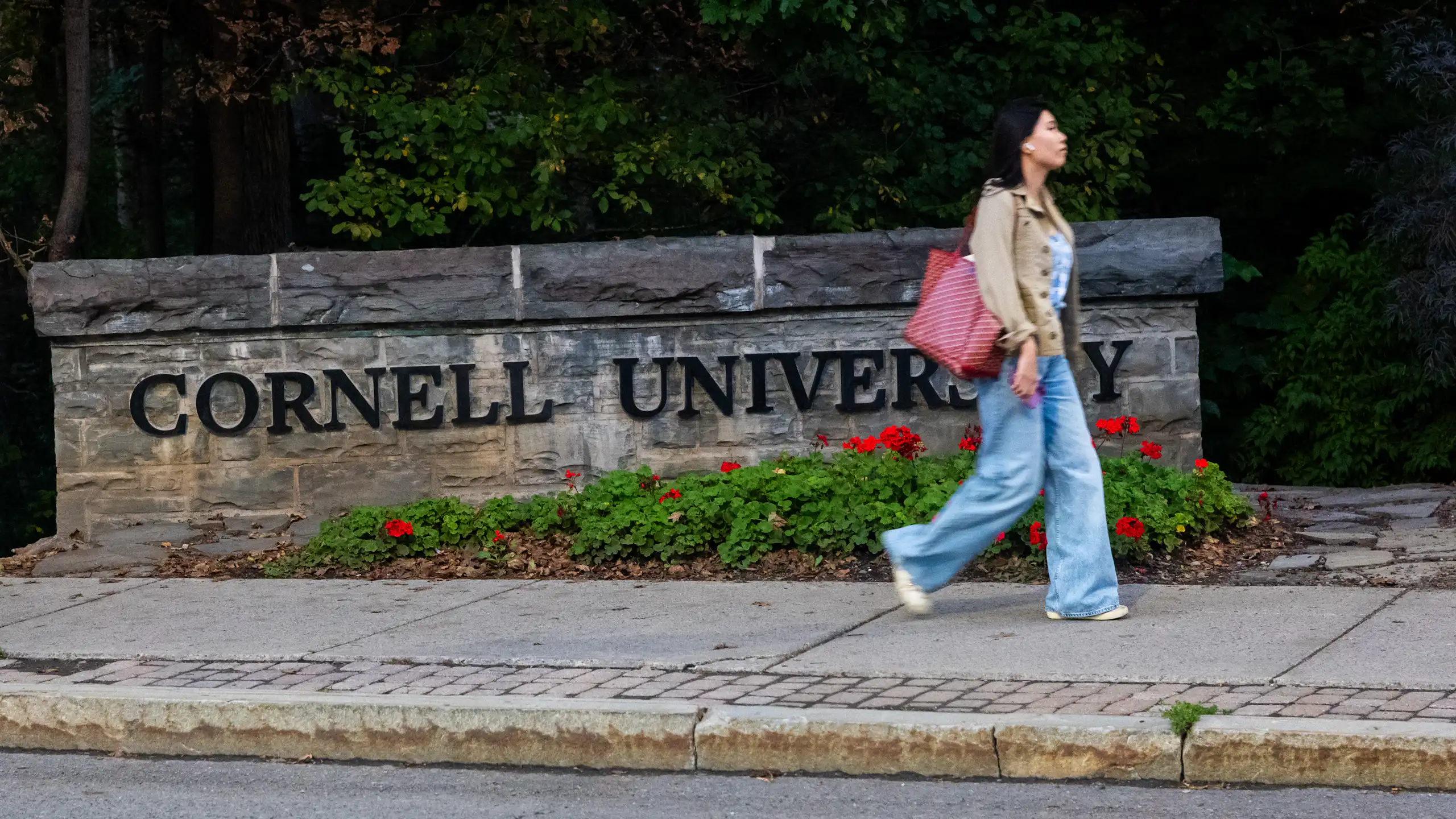A woman walks past a large sign saying Cornell University