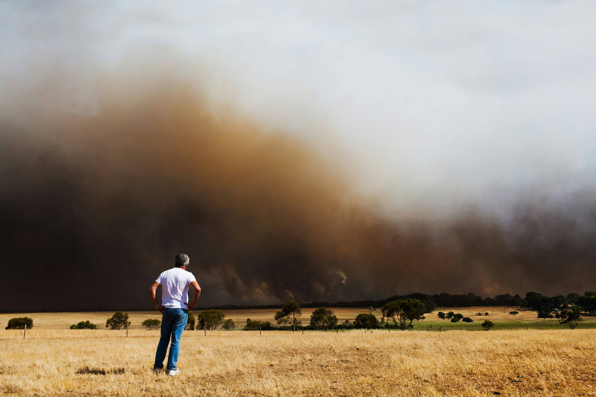 A man watches as a bushfire burns in a rural area.