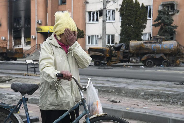 A woman pushing a bicycle and covering her eyes with her hand.