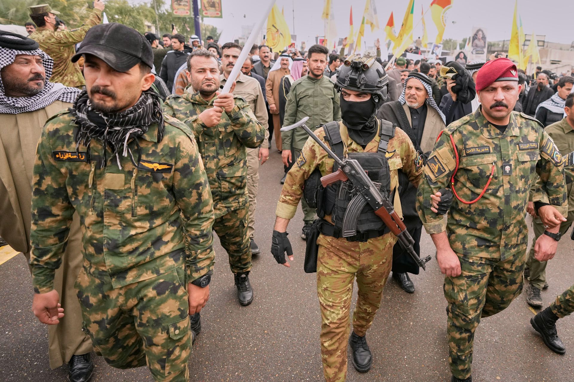 Iraqis in military uniforms, one wearing a balaclava, walk along a Baghdad street.