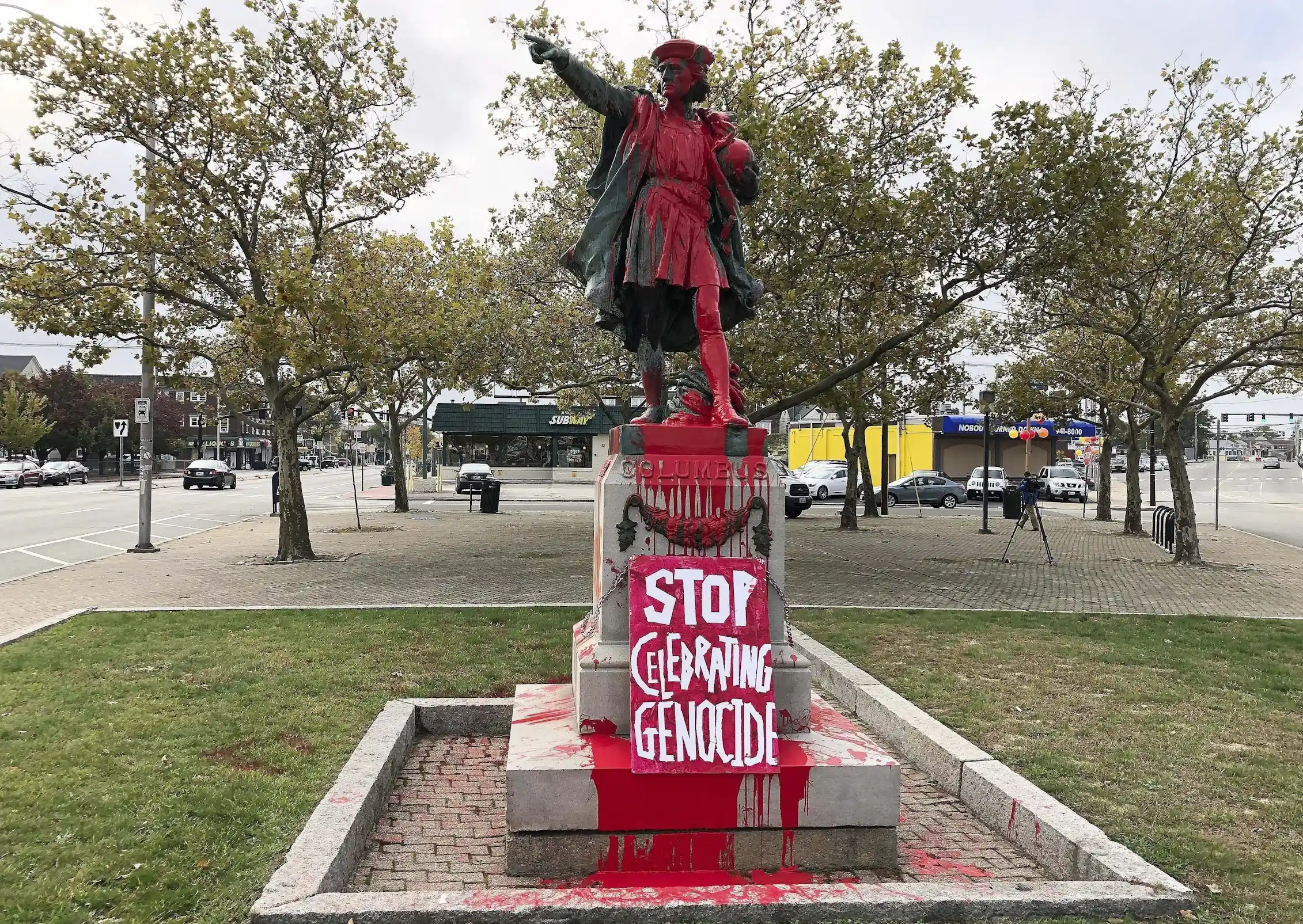 A statue of a man with an outstretched arm is covered in red paint and the words