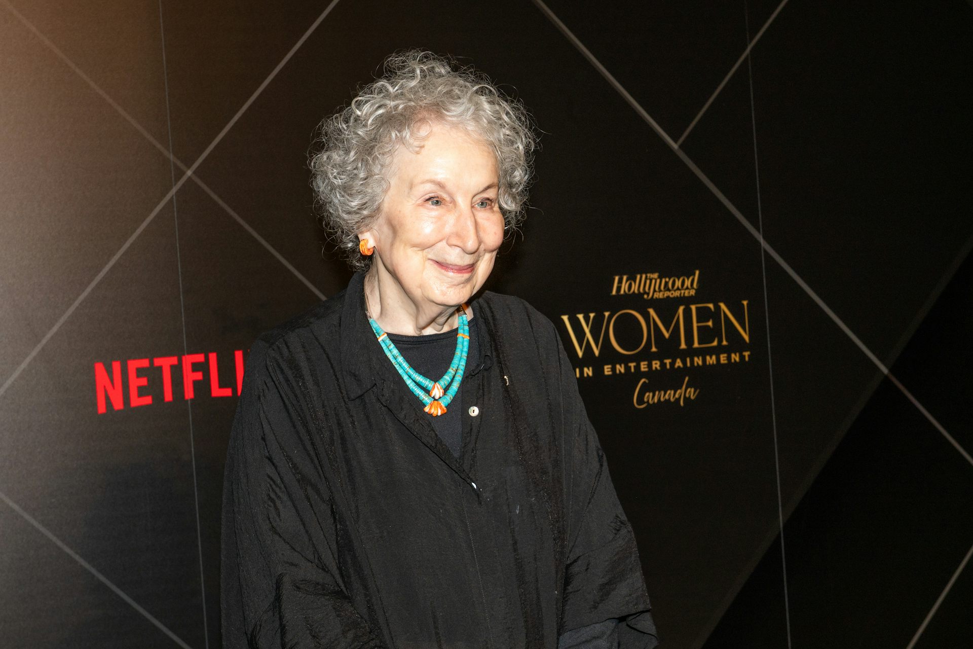A woman in a dark dress stands in front of a backdrop that says Hollywood and Netflix.