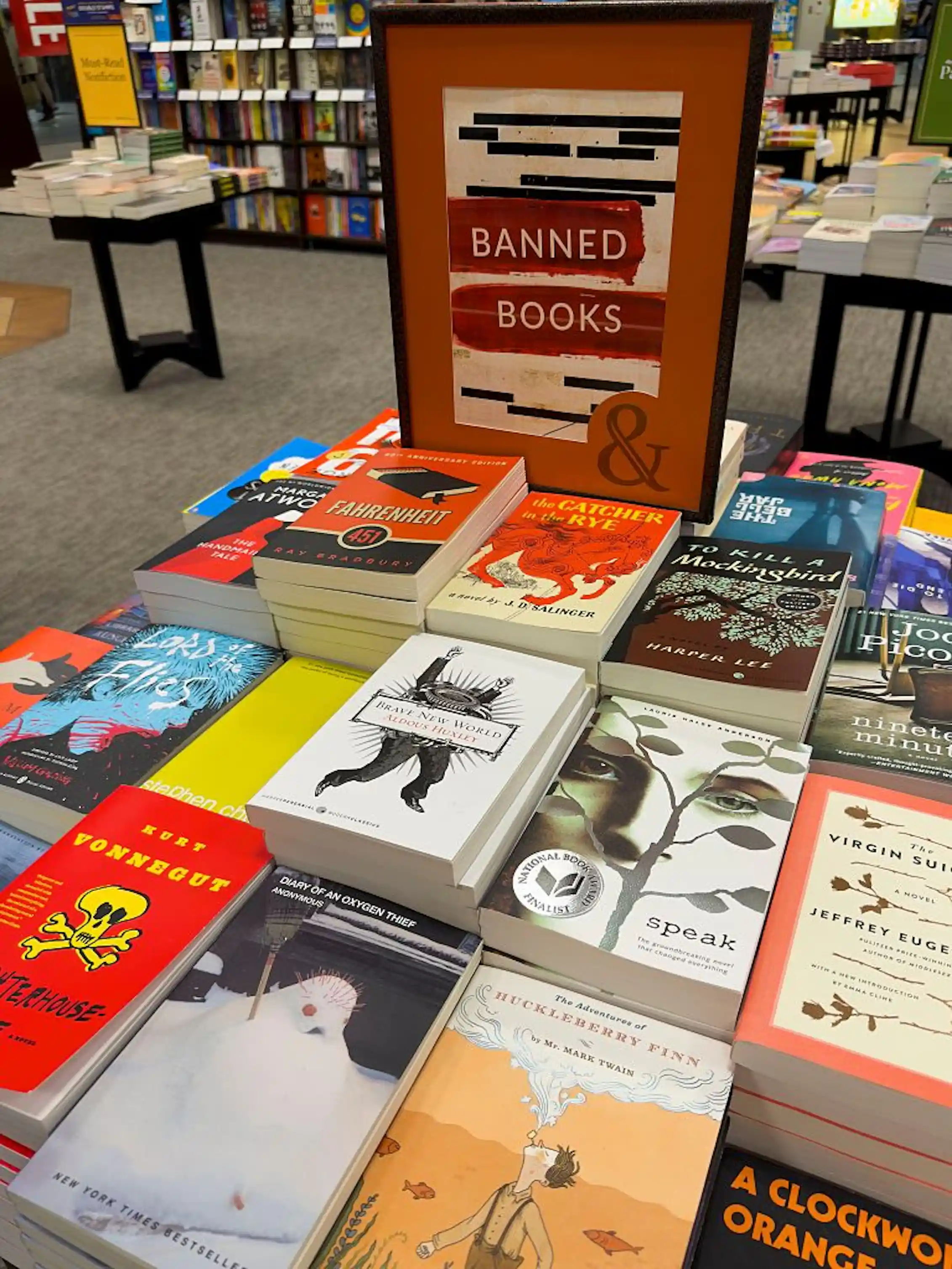 A table with stacks of colorful books surrounding a sign reading