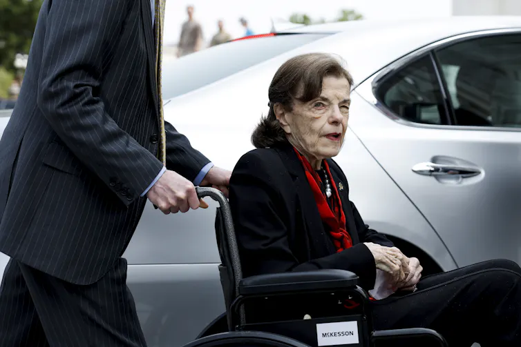 An ailing older woman is pushed in a wheelchair.