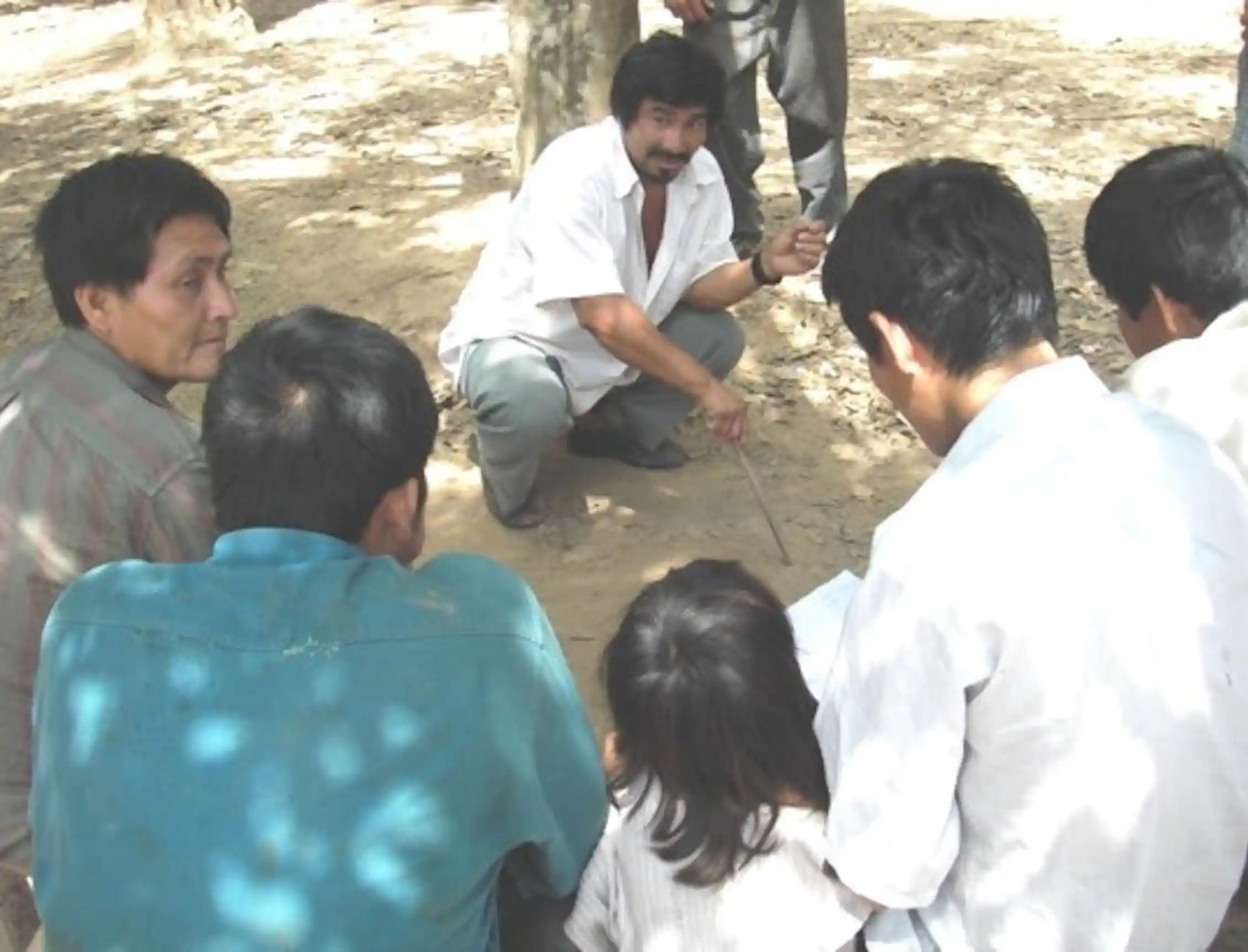 semi circle of people outside facing a man squatting on the ground