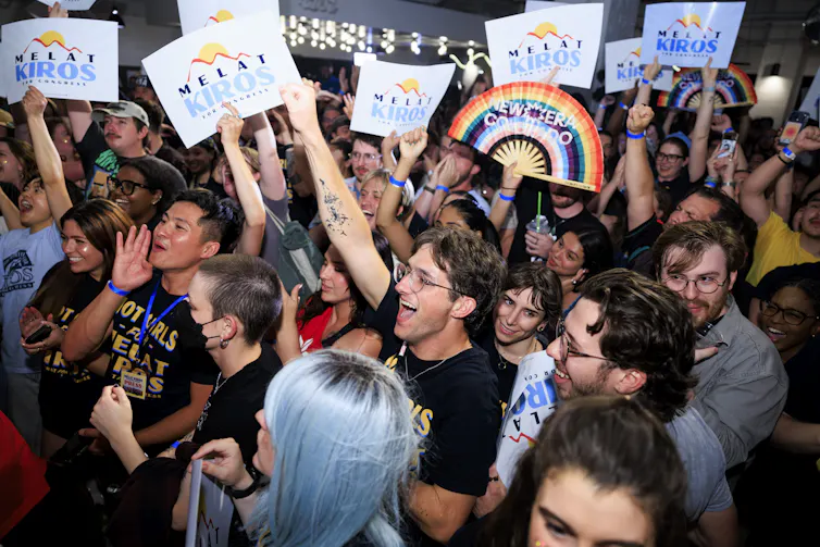 A crowd of mostly young people, many holding signs and looking excited and happy.