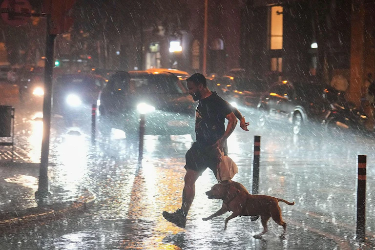 Un hombre cruza la calle corriendo con su perro bajo una intensa lluvia