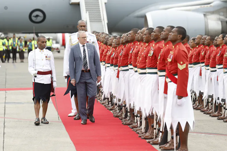 Prime Minister Anthony Albanese disembarks from a plane Nadi Airport and inspects a line of red-coated Fijian guards.